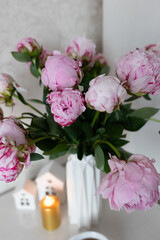 tea in a white cup, pink peonies, flowers and candles of golden color on a white background.Laptop, beautiful pink peony bouquet and notebook on white table background. minimalist home workspace. 