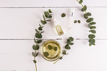 Cosmetic product based on natural eucalyptus oil on a wooden white background with eucalyptus branches and a bowl of organic oil. Top view