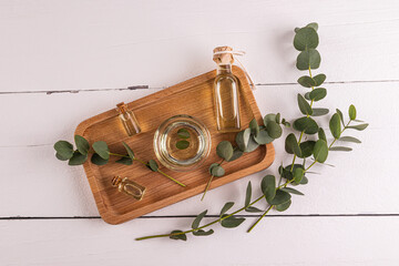 Natural eucalyptus oil in various glass bottles on a wooden tray with eucalyptus branches. Top view. White wooden background. Homemade cosmetics.