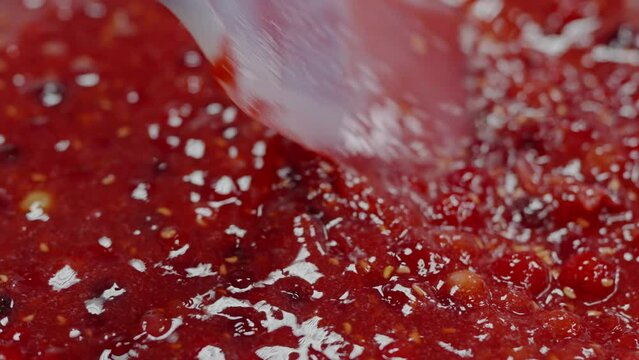A detailed close-up image of a shiny, textured surface of freshly made strawberry jam, highlighting the seeds and syrupy texture. Close-Up View of Glistening Strawberry Jam Spread