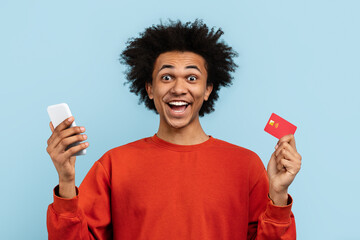 Guy holding phone and credit card on blue background