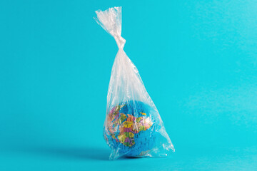 Earth globe in plastic bag on blue background. Minimal ecology concept.