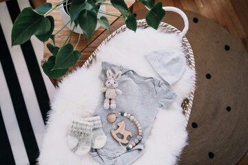Still life background of cute baby products - changing basket with baby bodysuit, newborn clothes, knitted rabbit and wooden toy. Minimalist style photography of baby shower, pregnancy announcement.