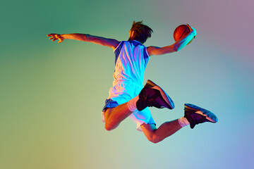 Competitive man, athlete in motion, training, playing basketball against gradient background in...