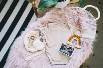 Baby changing basket with ultrasound image, baby bodysuit, soft and wooden toys. Still life of child products. Newborn background. Minimalist style photography of baby shower, pregnancy announcement.
