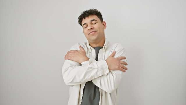 Confident, young arab man, smiling with positive self-love, hugging himself while wearing casual clothes isolated over white background.