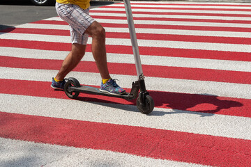 Detail of a man riding a non-electric kick scooter in a crosswalk