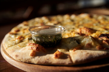 A delicious round pizza on a wooden tray with pesto sauce. A process of tasting eating traditional italian four cheeses pizza in outside restaurant terrace.Simple snack.Unhealthy food.Nutrition rules