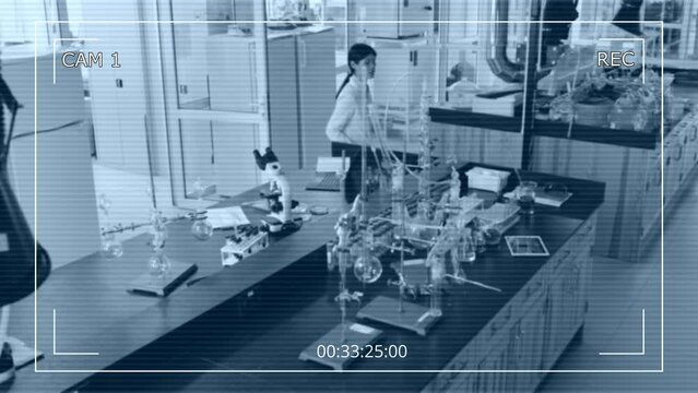 Full high angle CCTV camera shot of Asian female employee of research laboratory working alone - typing on laptop, then walking over to table and handling chemical liquids and reagents