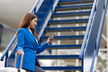 Asian businesswoman holding a bag is walking up the airplane stairs. Happy young female traveler...