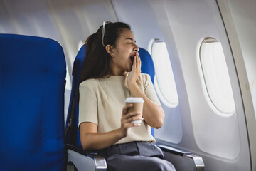 Young Asian female tourist traveling alone on a plane is drinking hot coffee and looking out the...