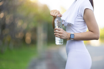 Attractive young Asian woman who is thirsty is drinking water while taking a break from jogging at...