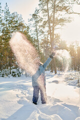 Excited kid in winterwear standing in snowdrift in natural environment on sunny winter day and having fun with snow