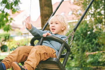 Outdoor portrait of adorable little boy having fun on swing on playground