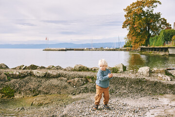 Outdoor portrait of happy and active toddler boy playing by the lake on a nice spring or autumn day
