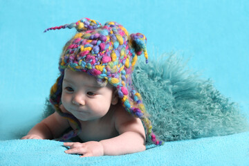 Cute little baby in a funny knitted hat on a sky blue background.
