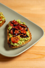 A plate of bruschettas topped with vibrant guacamole and cherry tomatoes sits on a restaurant table. The golden toasted bread contrasts beautifully with the fresh green guacamole and red tomatoes.