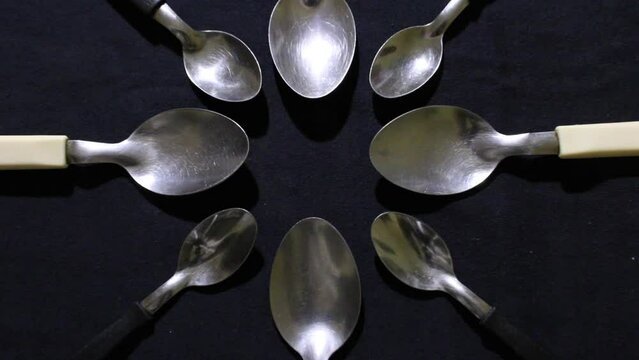 Cucharas grandes y peque&ntilde;as en c&iacute;rculo, son herramientas culinarias para comidas variadas,  forman un dise&ntilde;o de brillos y texturas  abstractos con fondo negro.
