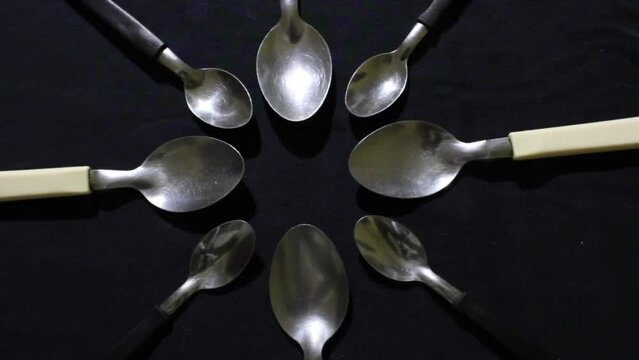 Cucharas grandes y peque&ntilde;as en c&iacute;rculo, son herramientas culinarias para comidas variadas,  forman un dise&ntilde;o de brillos y texturas  abstractos con fondo negro.