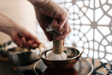 Closeup of ayurvedic massage practitioner male dipping cotton-wrapped herbal bundle into aromatic oil during prepare to Shirodhara treatment. Tranquil and serenity of aromatherapy recreation at salon.
