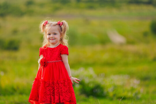 little girl in a red dress walks on the lawn