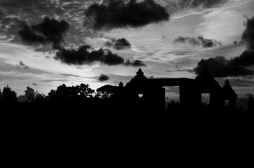 Silhouette of ancient buildings against a dramatic grayscale sky at sunset.