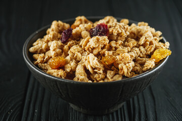 tasty crunchy granola with dried fruits on a black wooden rustic background