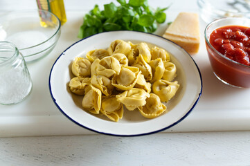 Ingredients for making pasta with tomato sauce on a white cutting board such as tortellini,...