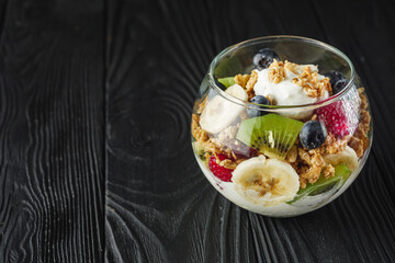 delicious crunchy granola dessert with berries and fruits on a black wooden rustic background
