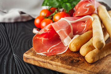 crispy grisini with prosciutto on a black wooden rustic background