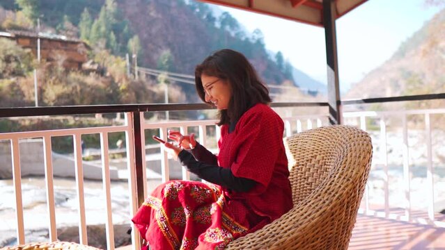 Beautiful Indian woman sitting on a blue chair and using smartphone or cell phone in mountain resort at Manali, Himachal Pradesh, India. woman holding cellphone, swiping photos on social media.