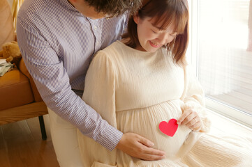 妊娠中のお腹の前でハートをもつ女性