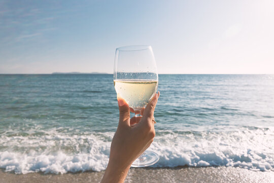Female hand with glass of wine on the beach. Summer vacations concept.