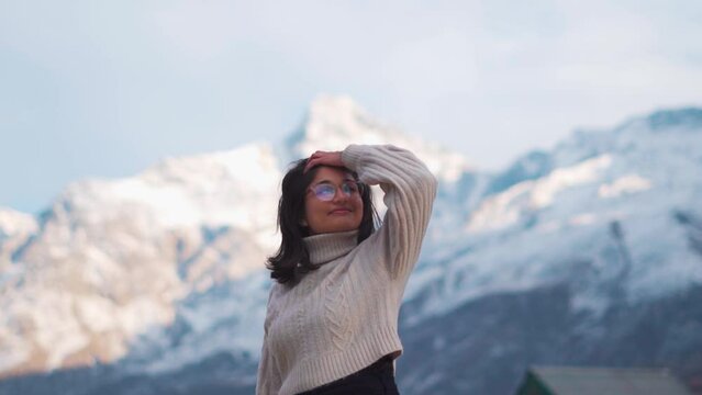 Portrait of smiling Teenager Indian girl standing against snowy mountains in Lahaul, himachal Pradesh, India. Girl wearing warm sweater in cold weather of mountains. Holiday and vacation concept. 