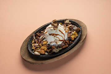 Piece of Brownie, Vanilla Ice cream Dry Nuts and Choclate in a wooden base iron plate