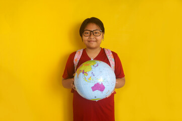 Portrait of Asian little girl student wearing eyeglasses and backpack, holding globe isolated over...