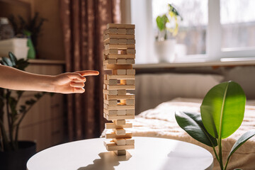 A child slides a wooden block of Jenga game on a white table under sunlight.