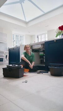 Vertical video portrait of female plumber fixing waste disposal unit in domestic kitchen  - shot in slow motion