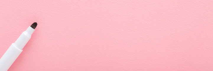 Black white color pen on light pink table background. Pastel color. Closeup. Wide banner. Empty place for text. Top down view.