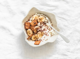Delicious breakfast - cottage cheese with greek yogurt, banana, crackers and chocolate on a light background, top view