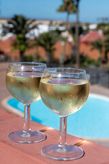 Glasses of cold white wine on roof terrace served outdoor in Corralejo, Fuerteventura in sunny day, pool with blue water