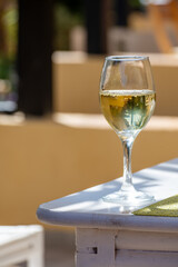 Glass of cold white wine on white terrace table outdoor in sunny day