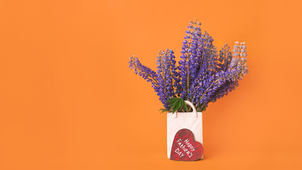 Bouquet of fresh lupine flowers in white vase shaped like bag and wooden red heart with white...