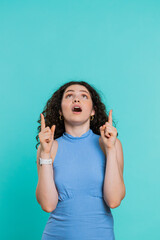Young woman showing thumbs up, pointing empty place above head, overhead advertising area for commercial text, copy space for goods promotion advertisement. Girl isolated on blue background. Vertical