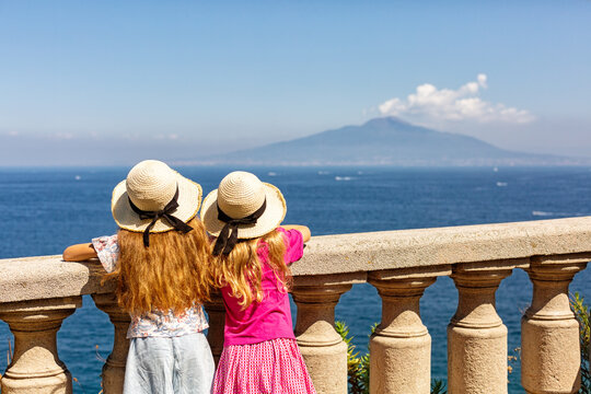 Sorrento, Italy - August 15th, 2023. Two tourist gitls in heats looking at Mount Vesuvius from Coastline of Sorrento, sea, Gulf of Naples, Italy. Selective focus. No visible faces.