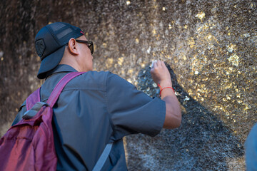 Male tourists pay their respects by covering the giant rocks with gold leaf at Khao Khitchakut National Park, Chanthaburi, Thailand.
