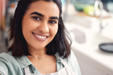 Fototapeta premium Selfie, kitchen and woman with smile, portrait and apron for cooking, catering and small business in home. Happiness, service and industry of food, hospitality and chef in apartment and confidence