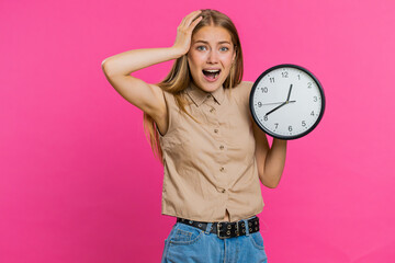 Woman with anxiety checking time on clock, running late to work, being in delay, deadline. Blonde busy girl looking at hour, minutes, worrying to be punctual isolated on pink studio background