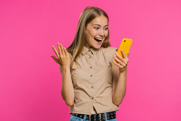 Happy excited joyful woman girl use smartphone typing browsing shouting say wow yes found out great big win, good news, lottery goal achievemen, celebrating success, winning game on pink background