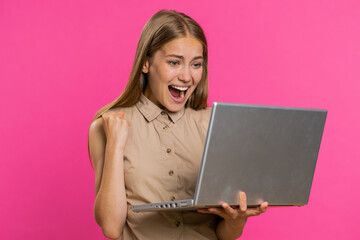 Overjoyed happy young woman with laptop scream in delight raise hand in triumph winner gesture celebrate success win victory money in lottery. Excited girl get online good news on pink background
